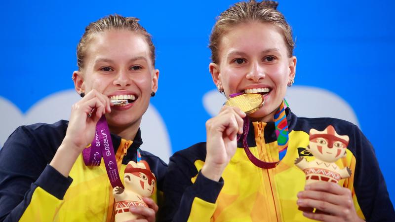 two female Para swimmers on the podium biting their medals