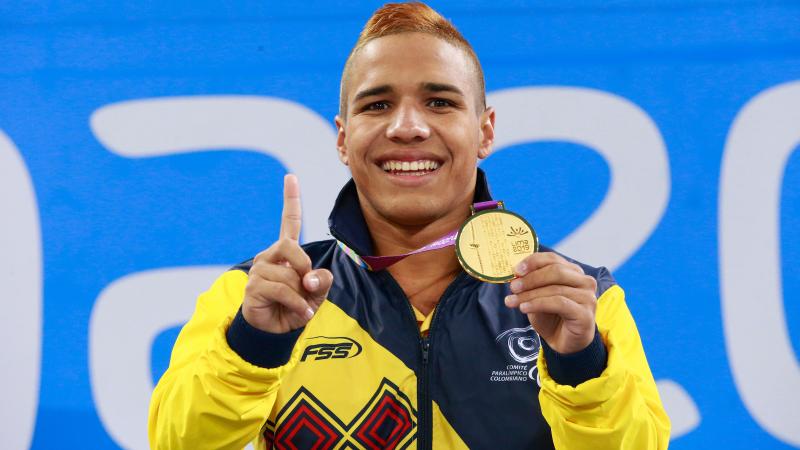 a male Para swimmer holds up his gold medal