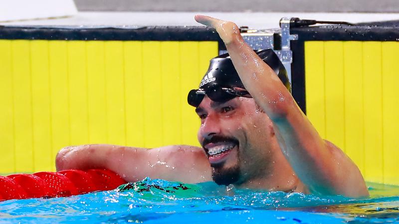 a male Para swimmer raises his arm in celebration in the pool