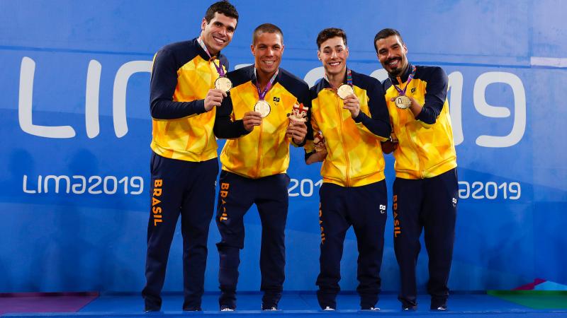 four male Para swimmers standing on the podium holding their gold medals