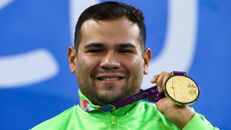 a male Para swimmer holds up his gold medal