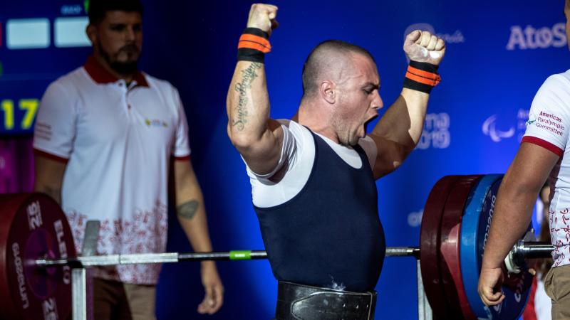 a male powerlifter roars and raises his fists after his lift