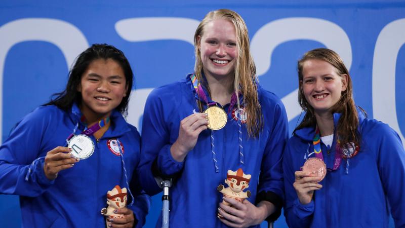 three female Para swimmers on the podium holding up their medals