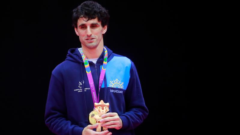 a male judoka stands on the podium with his gold medal