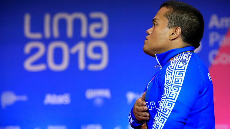 a male powerlifter with his hand over his heart singing the national anthem