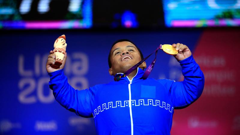 a male powerlifter holds up his gold medal