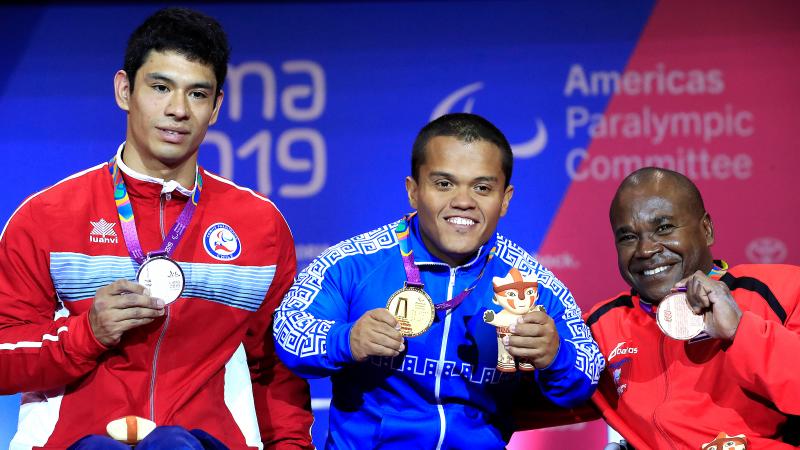 three male powerlifters on the podium holding up their medals