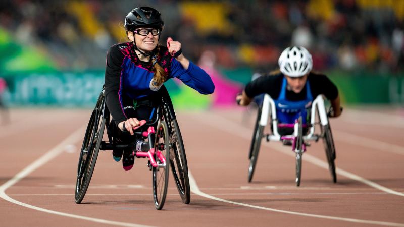 a female wheelchair racer clenches her fist as she crosses the finish line