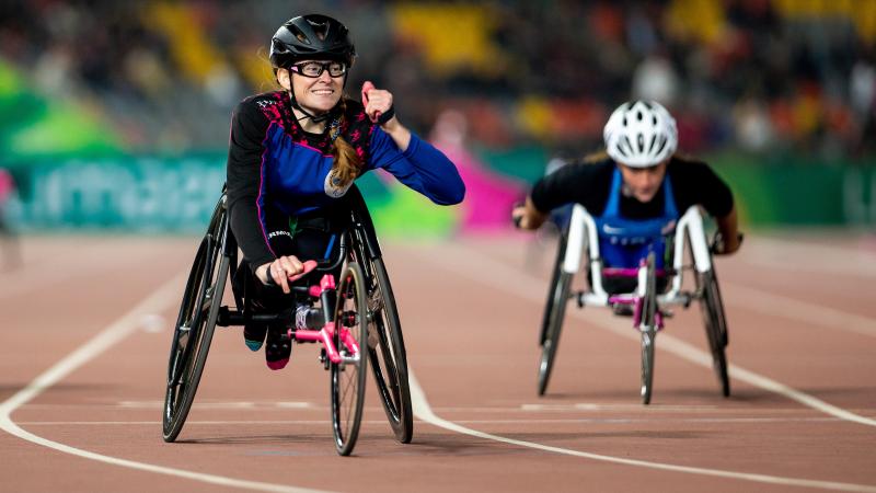 a female wheelchair racer clenches her fist as she crosses the finish line