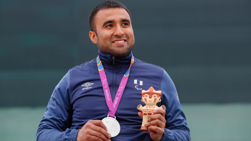 a male Para shooter holding a silver medal and smiling
