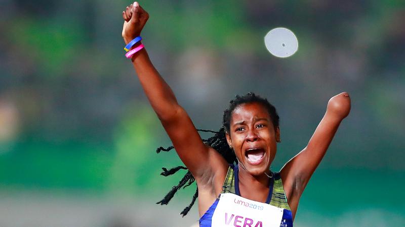 a female Para athlete raises her arms in celebration on the finish line