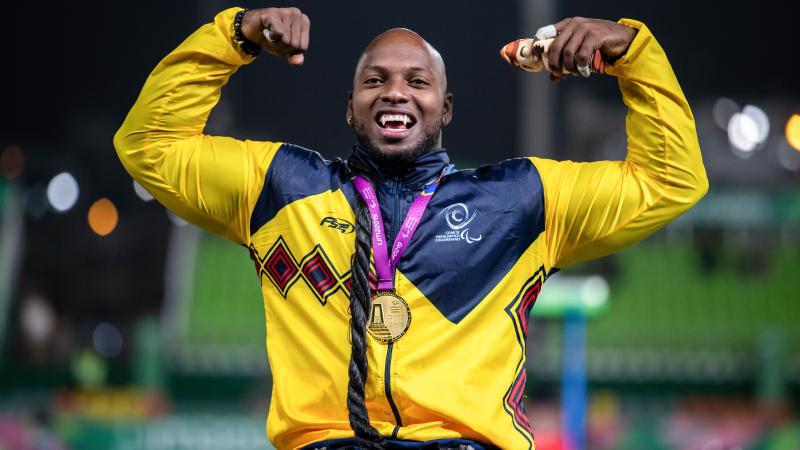 a male wheelchair athlete with a gold medal round his neck raises his arms