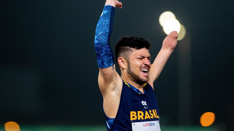 a male Para athlete throws his arms up in the air in celebration