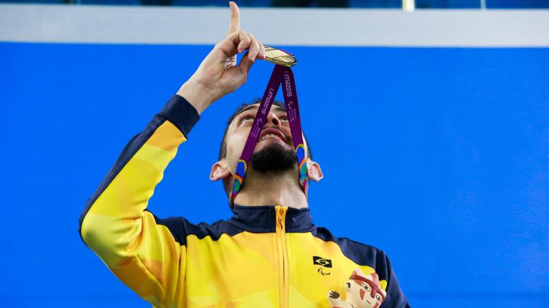 a male Para swimmer with a gold medal round his neck points to the sky