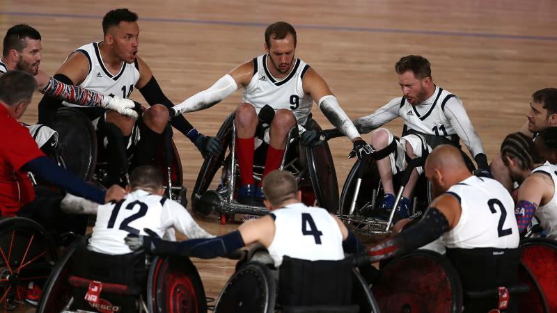 a group of male wheelchair rugby players in a circle holding arms