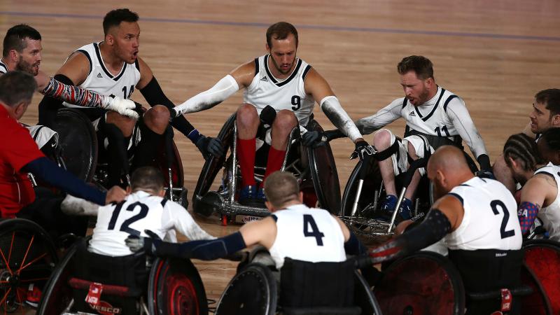 a group of male wheelchair rugby players in a circle holding arms