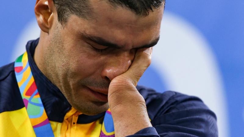 a male Para swimmer wiping away tears on the podium