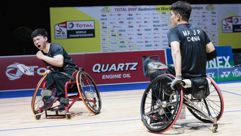 Two male Chinese badminton players in wheelchairs celebrate a point