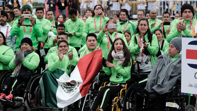 a group of Para athletes in Mexican kit cheer and wave Mexico flags