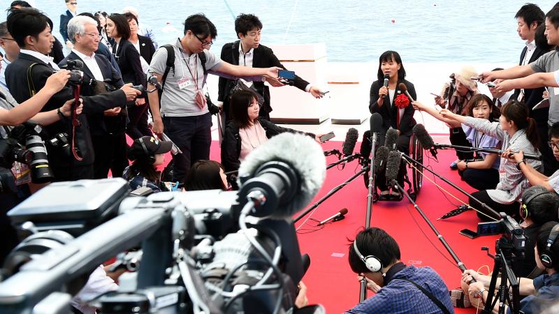 Japanese woman in wheelchair surrounded by media