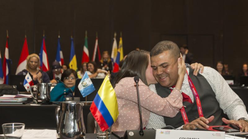 a man sitting at a desk smiling and being hugged by a woman