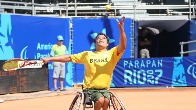 male wheelchair tennis player tosses the ball to serve on a clay court