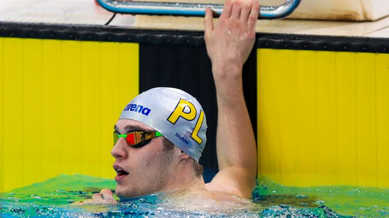 A male Para swimmer holds onto the pool wall at the end of a race