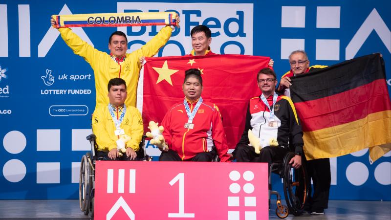 Three boccia athletes and their assistants pose on podium 