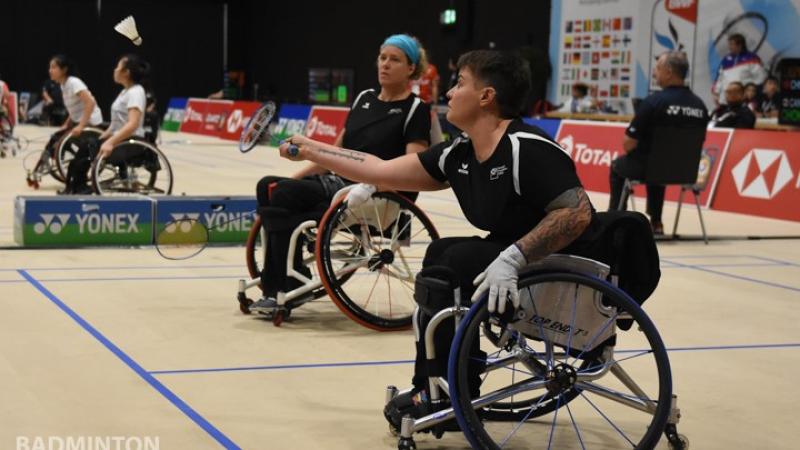 Two females in wheelchairs play badminton 