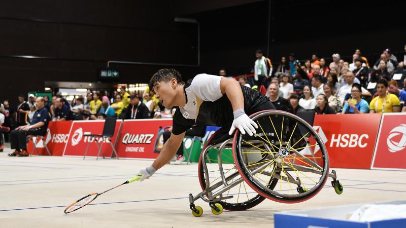 South Korean man in wheelchair leans over to hit the badminton birdie