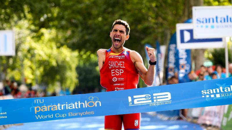 Man with right arm impairment celebrates while crossing the finish line tape