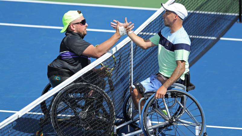two male wheelchair tennis players shake hands at the net