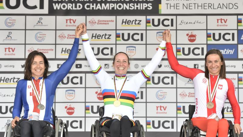 Three wheelchair cyclists hold hands on podium