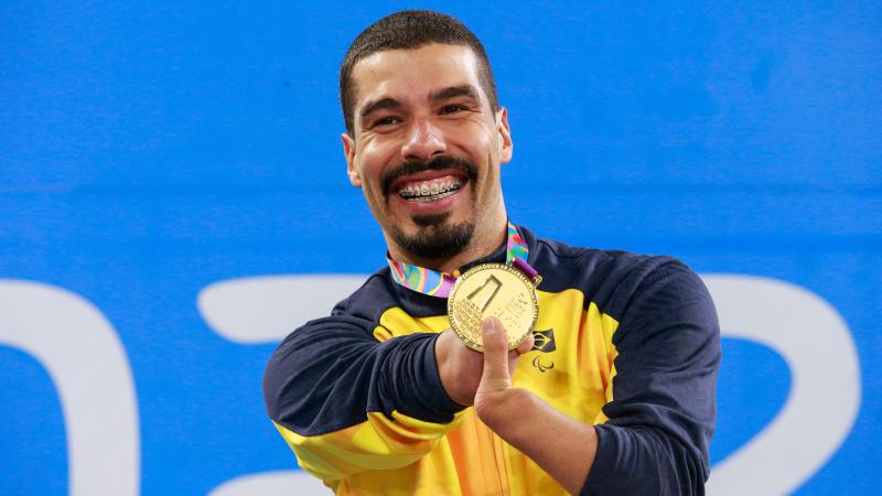 a male Para swimmer holds up his gold medal