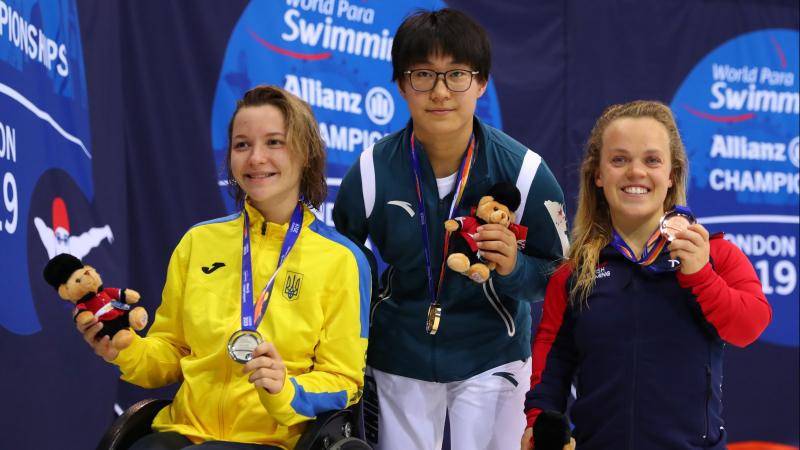 three female Para swimmers on the podium holding up their medals