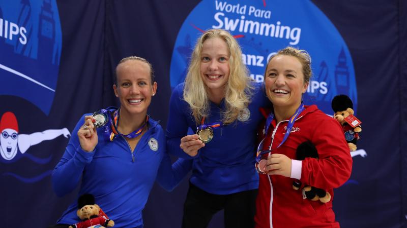 Three female swimmers pose on podium