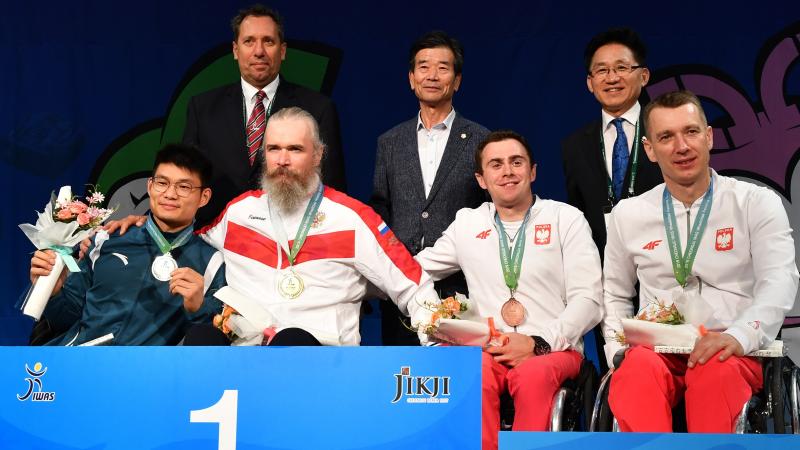 Four men in wheelchairs in a podium with three standing men behind them