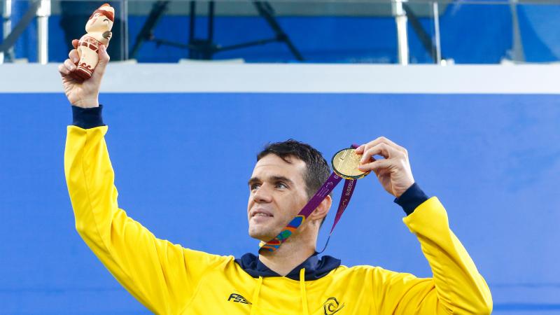 a male Para swimmer holds up his gold medal