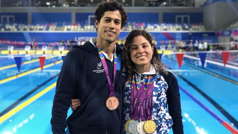 a male and female Para swimmer by the pool with their arms round eachother