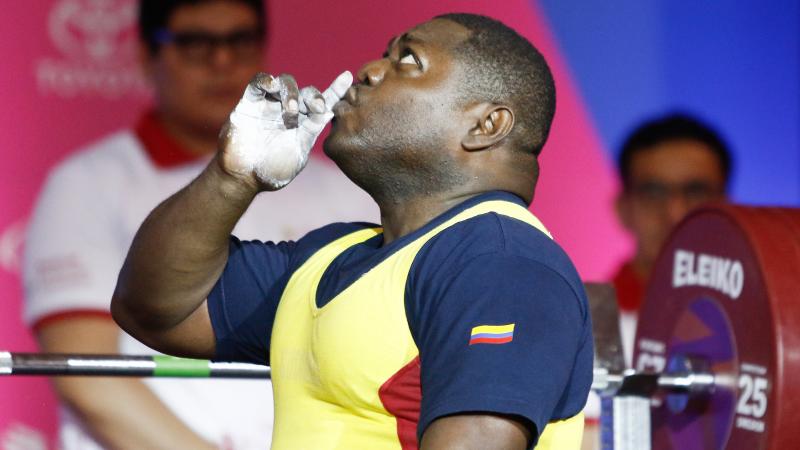a male powerlifter kisses his finger and looks to the sky