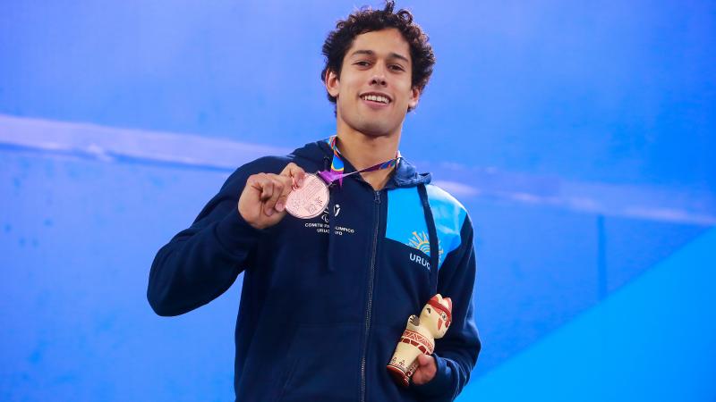 a male Para swimmer holds up his bronze medal