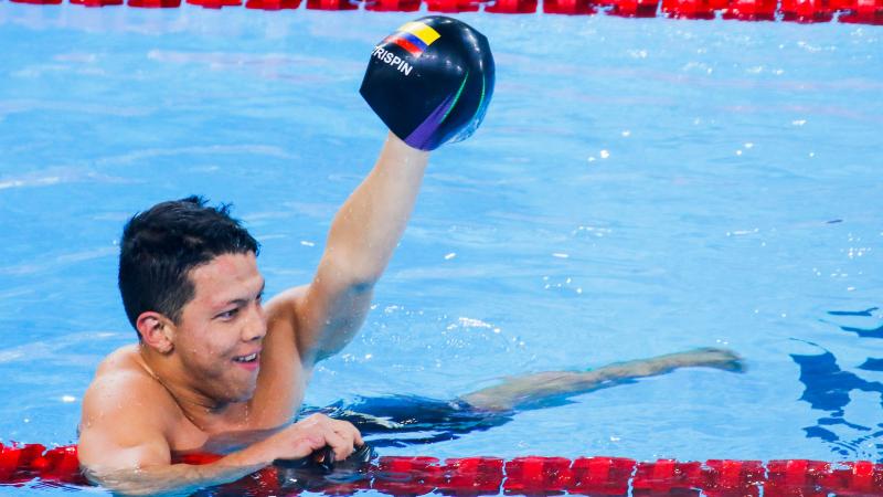 a male Para swimmer holds up his swimming cap 