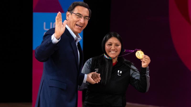 a female wheelchair badminton player with her gold medal and the President waving