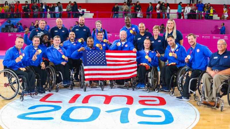 a group of male wheelchair basketball players holding their gold medals and the USA flag