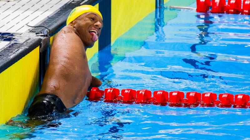 a male Para swimmer with no arms leaning on the lane rope