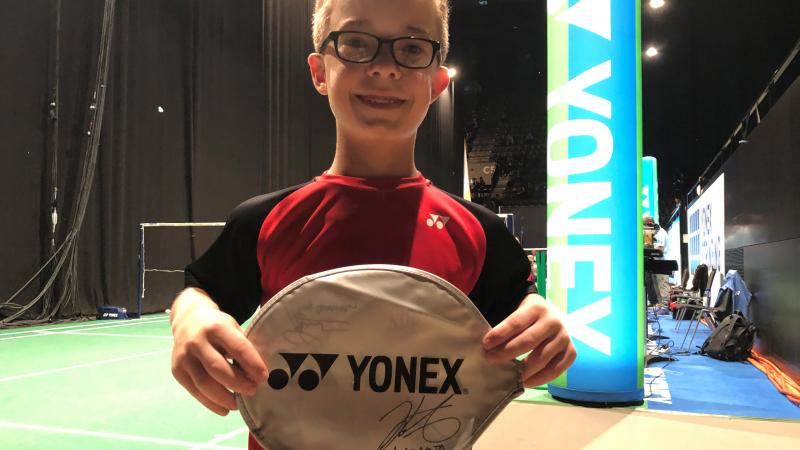 a male Para badminton player holds up a signed case