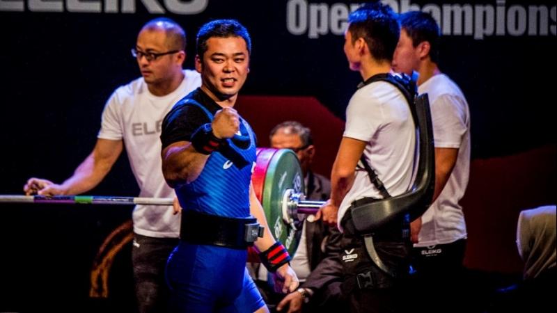 A male Para powerlifter celebrating with three assistants in the background