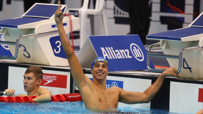 a male Para swimmer raises his arm in celebration in the pool