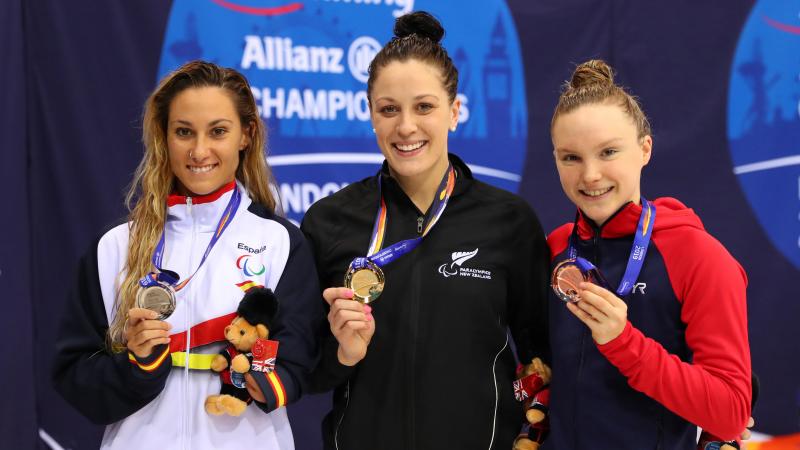 three female Para swimmers on the podium holding up their medals