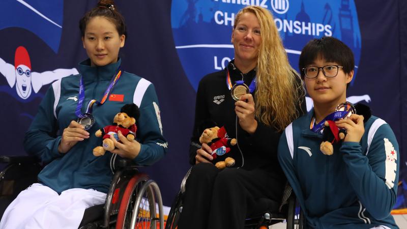 three female Para swimmers on the podium holding up their medals